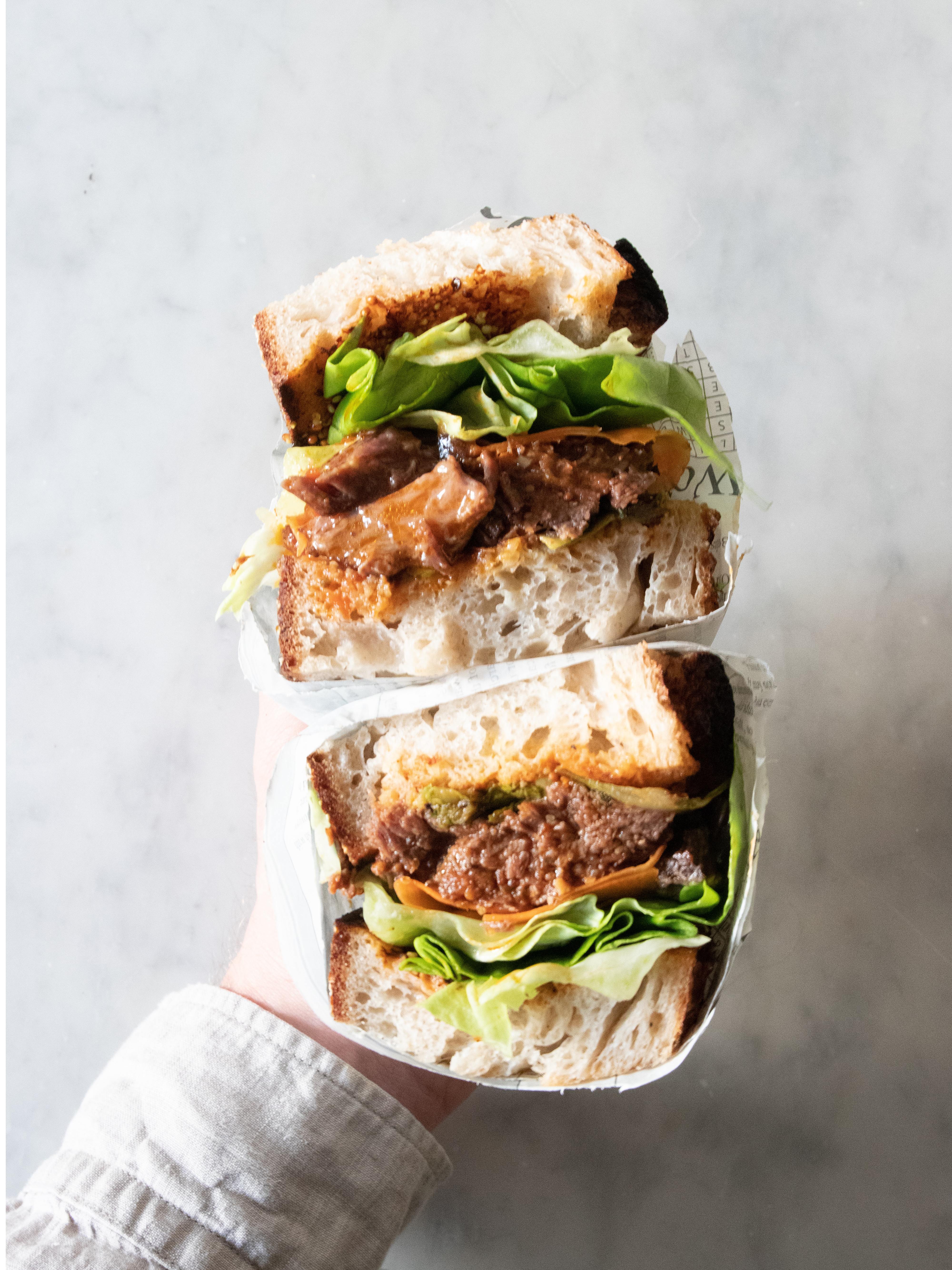 Hand holding a cheeseburger sandwich with lettuce in front of a white background.