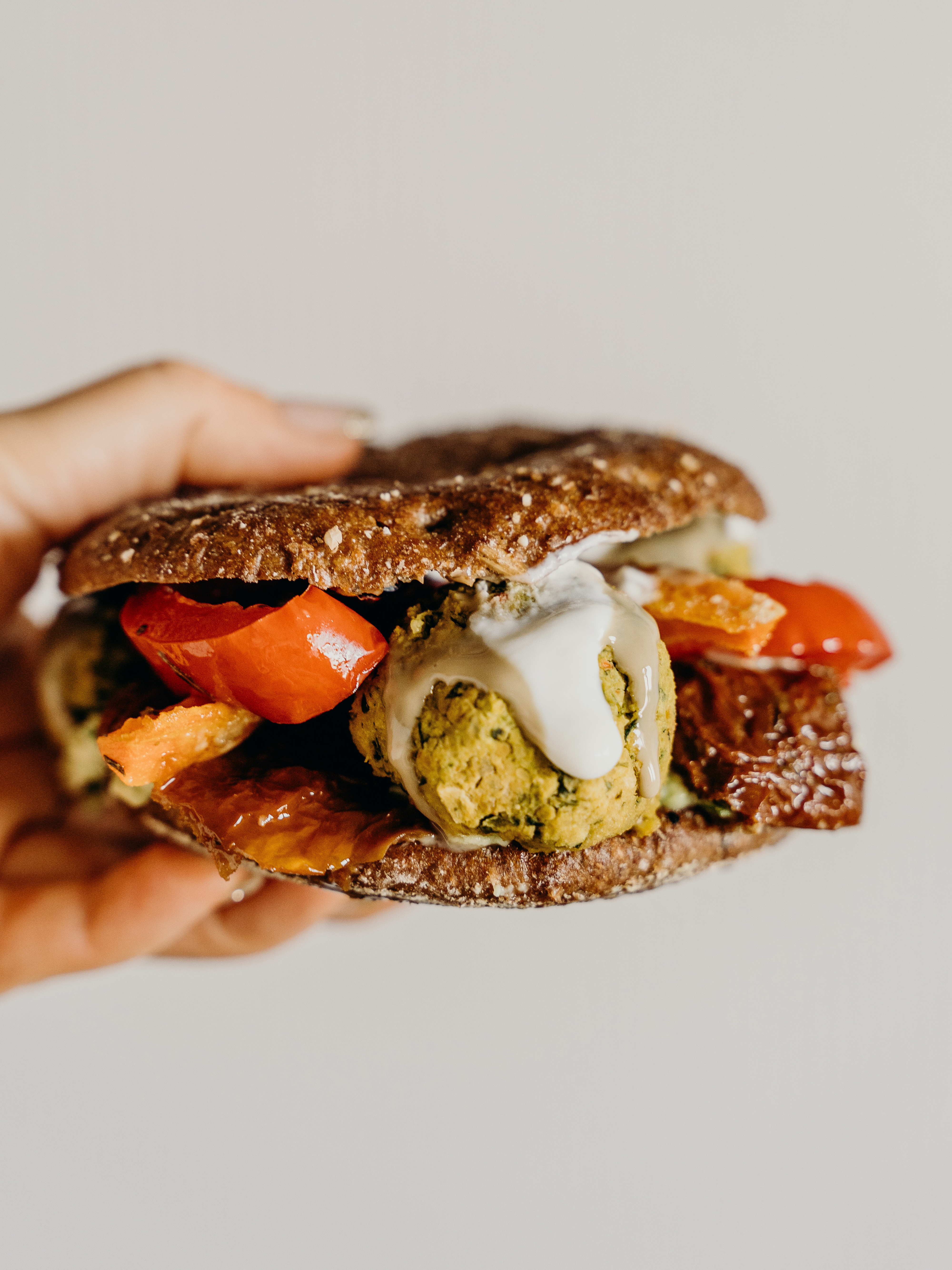 Hand holding a sandwich with tomatoes, falafel, and white sauce.